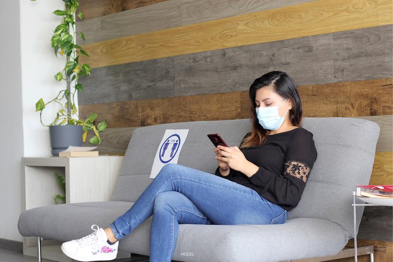 Woman sitting in waiting room, wearing a face mask.